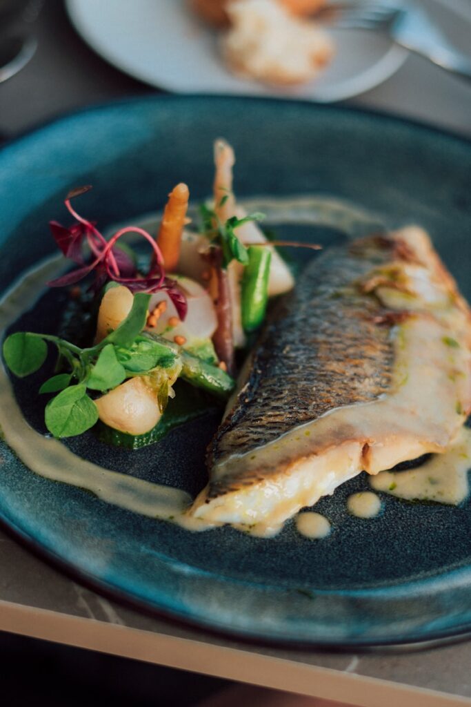 a blue plate topped with a piece of fish next to a salad