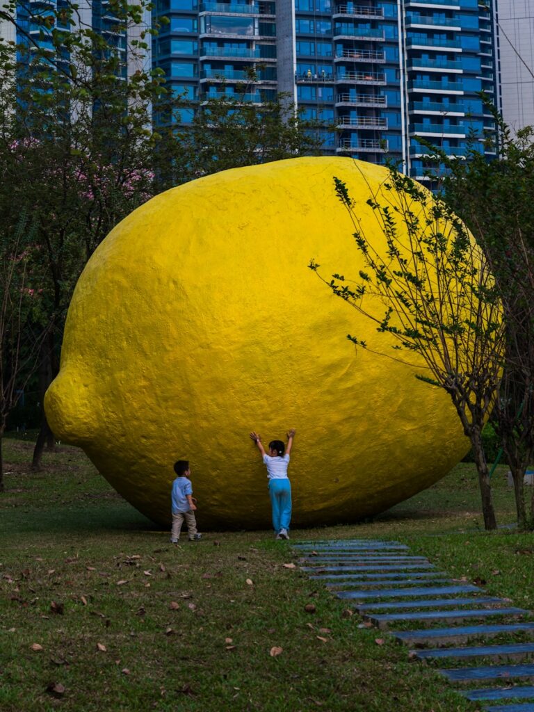 Two children stand by a giant yellow lemon sculpture.