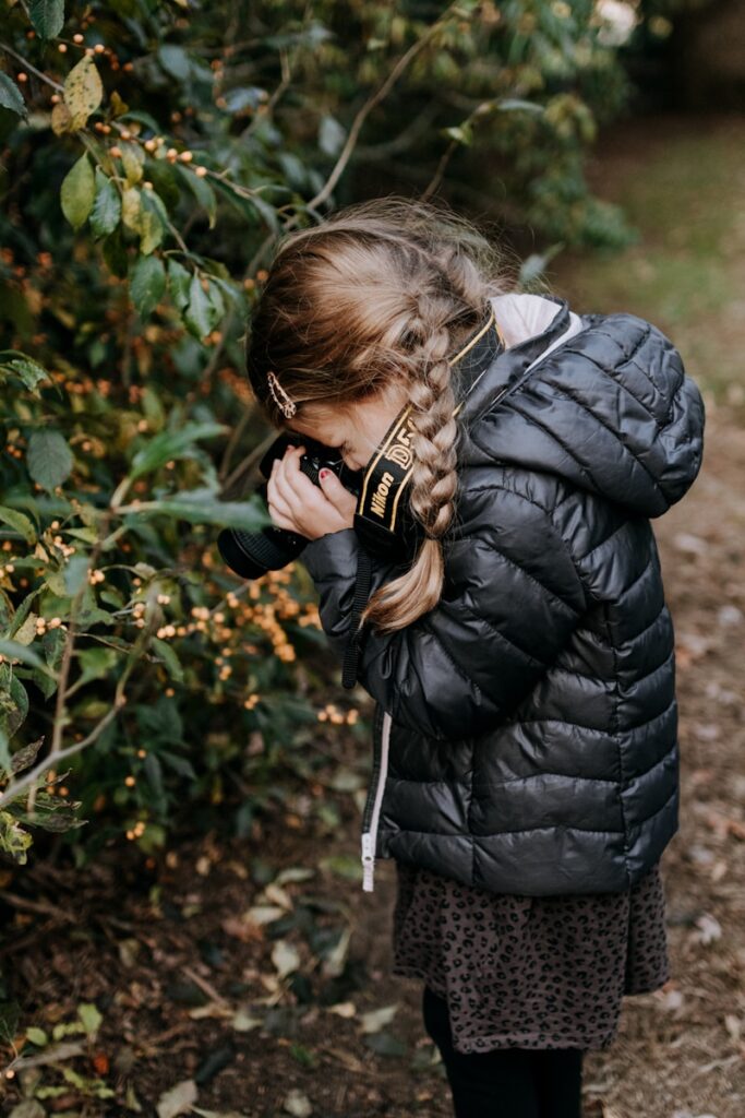 a little girl standing in front of a bush talking on a cell phone