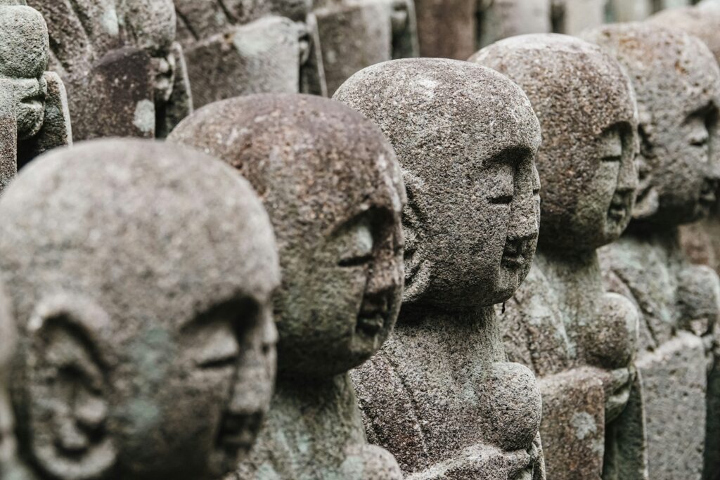Row of weathered stone jizo statues in a garden.
